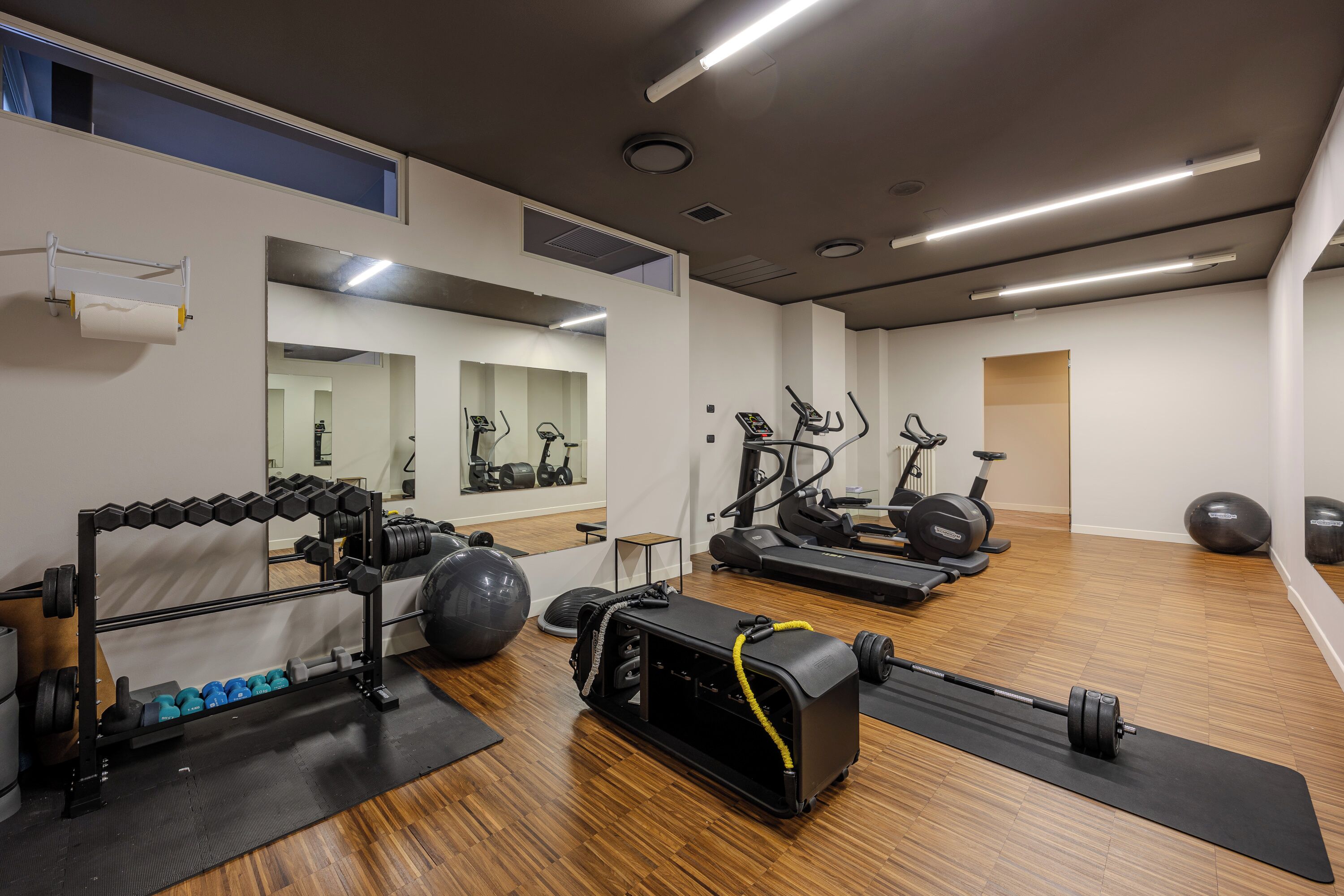 A gym with exercise equipment, a mirror, and a wooden floor.