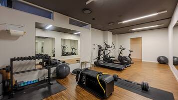 A gym with exercise equipment, a mirror, and a wooden floor.