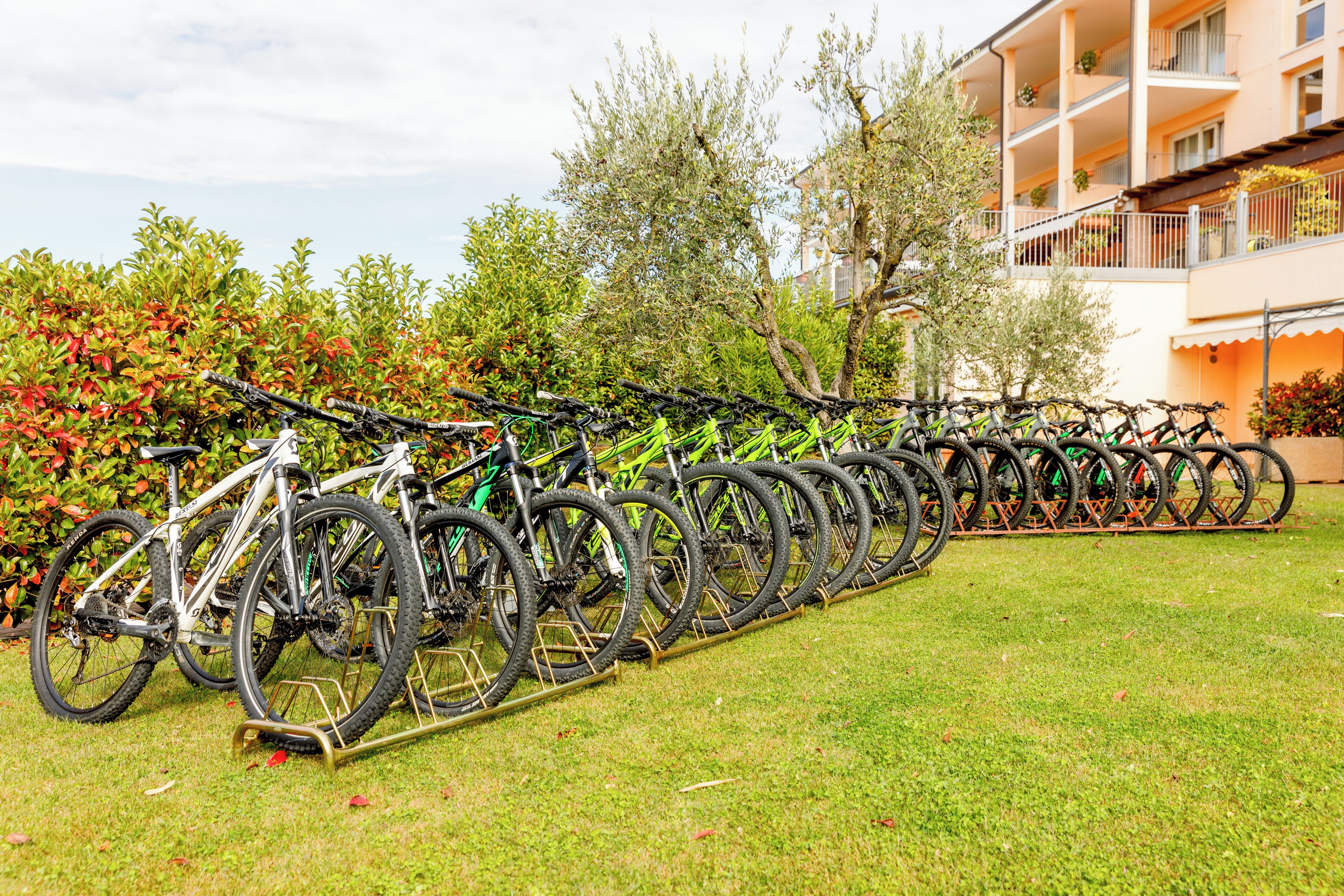 A row of bicycles parked on a grassy lawn in front of a building with balconies and windows.