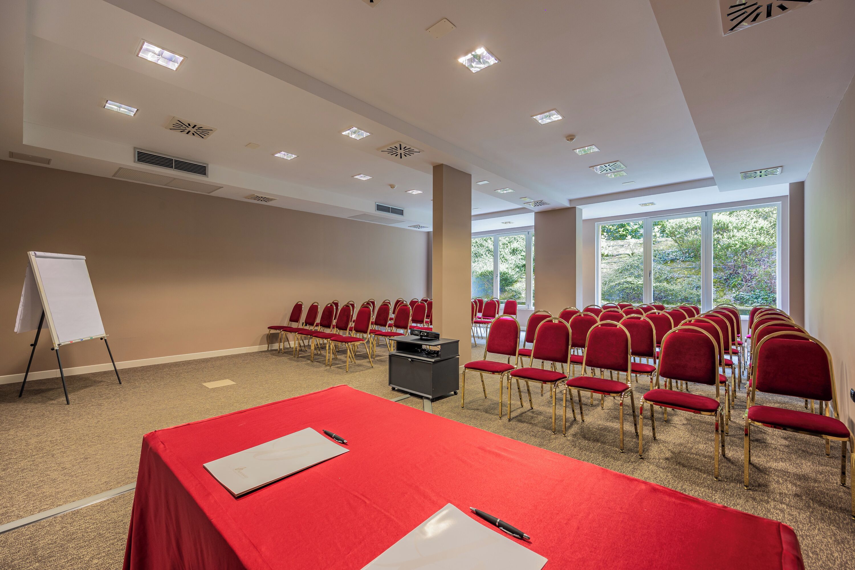 A conference room with a red table, whiteboard, and rows of red chairs.