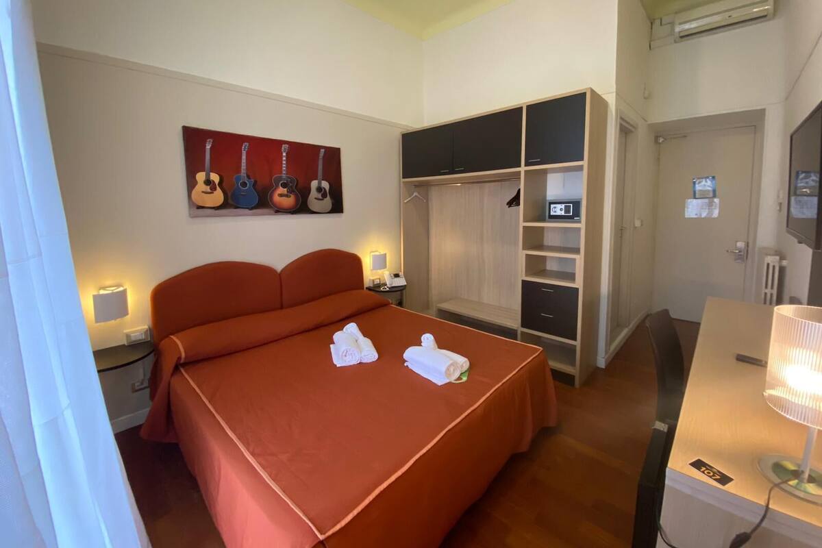 A hotel room with a large bed, a wardrobe, a desk, and a wall-mounted TV.
