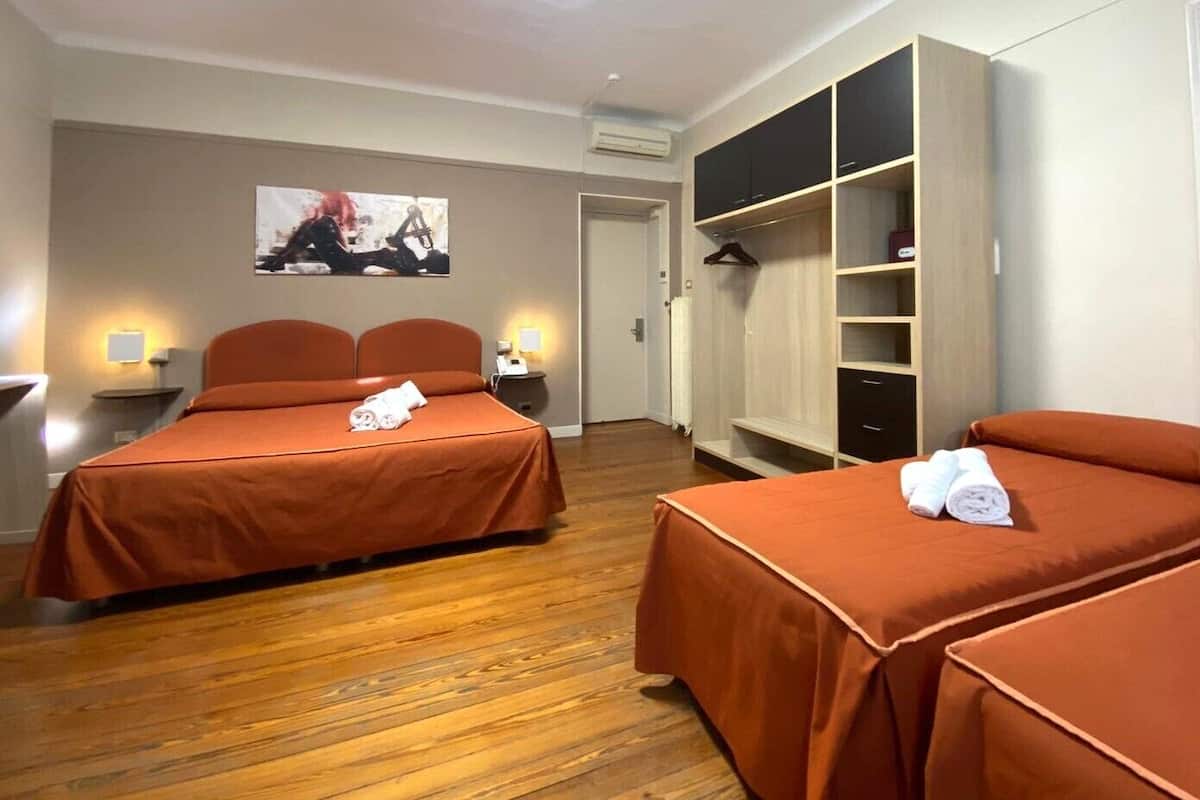A hotel room with two beds, a wardrobe, a desk, and a TV.