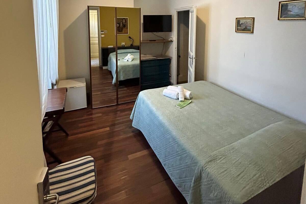 A hotel room with a bed, a desk, a chair, a mirror, a television, and a small window.