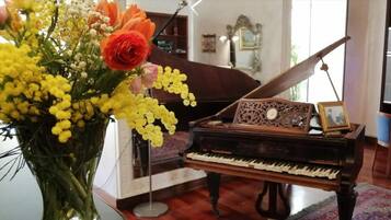A grand piano in a room with a large window, a vase of flowers, and a framed picture on the piano.