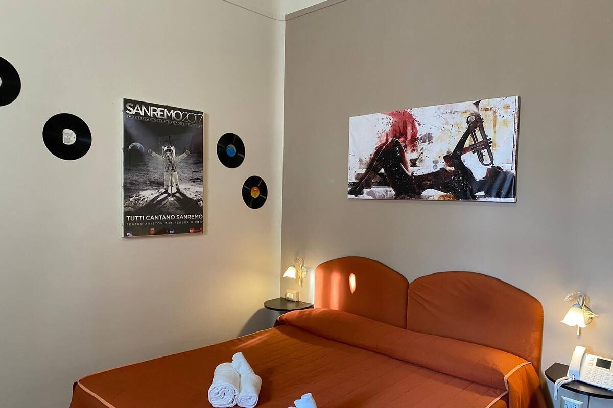 A hotel room with a bed, two bedside tables, a wall-mounted lamp, and a poster on the wall.