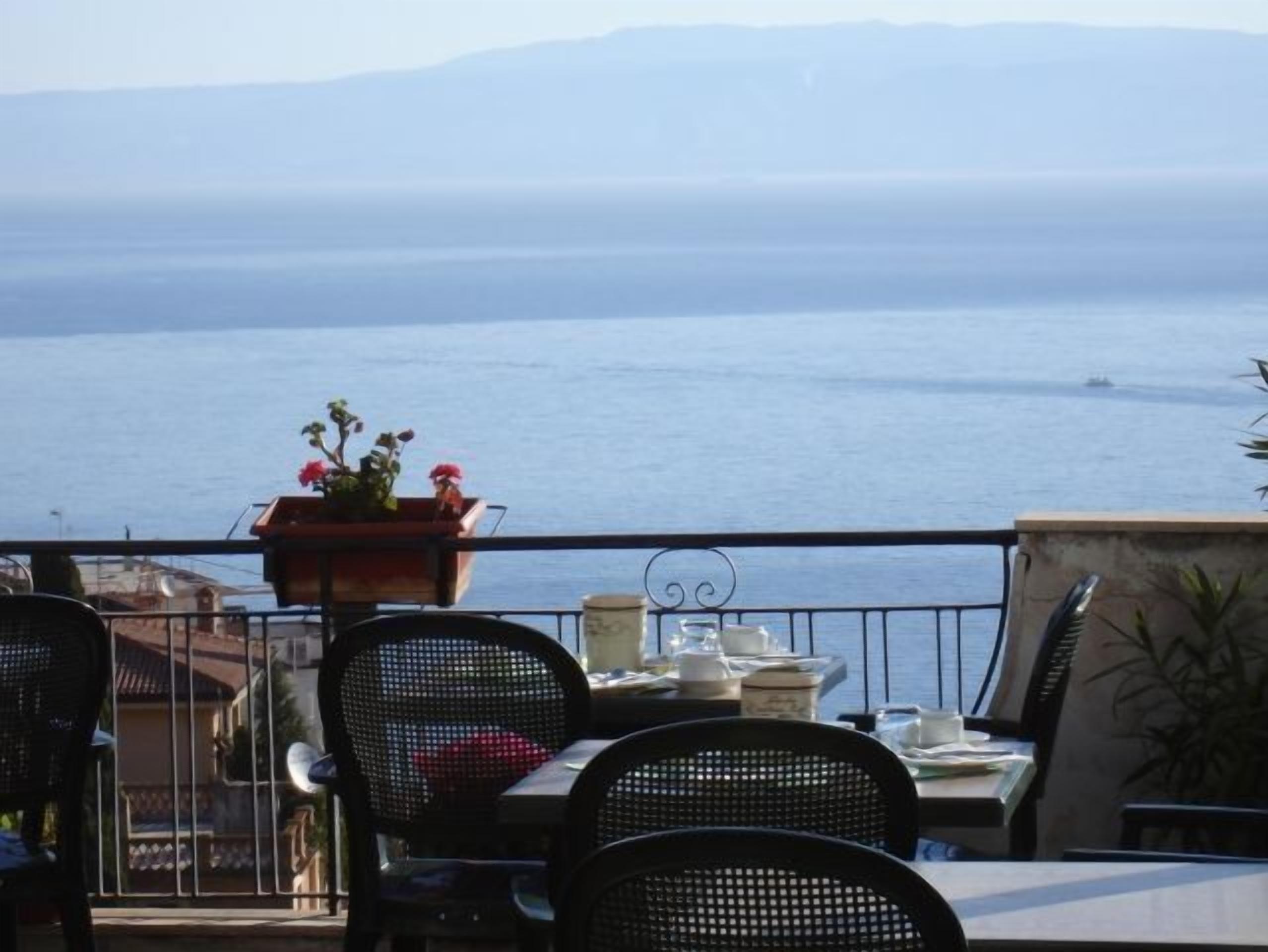 Eine Terrasse mit Tisch und Stühlen mit Blick auf ein ruhiges Meer und entfernte Berge.