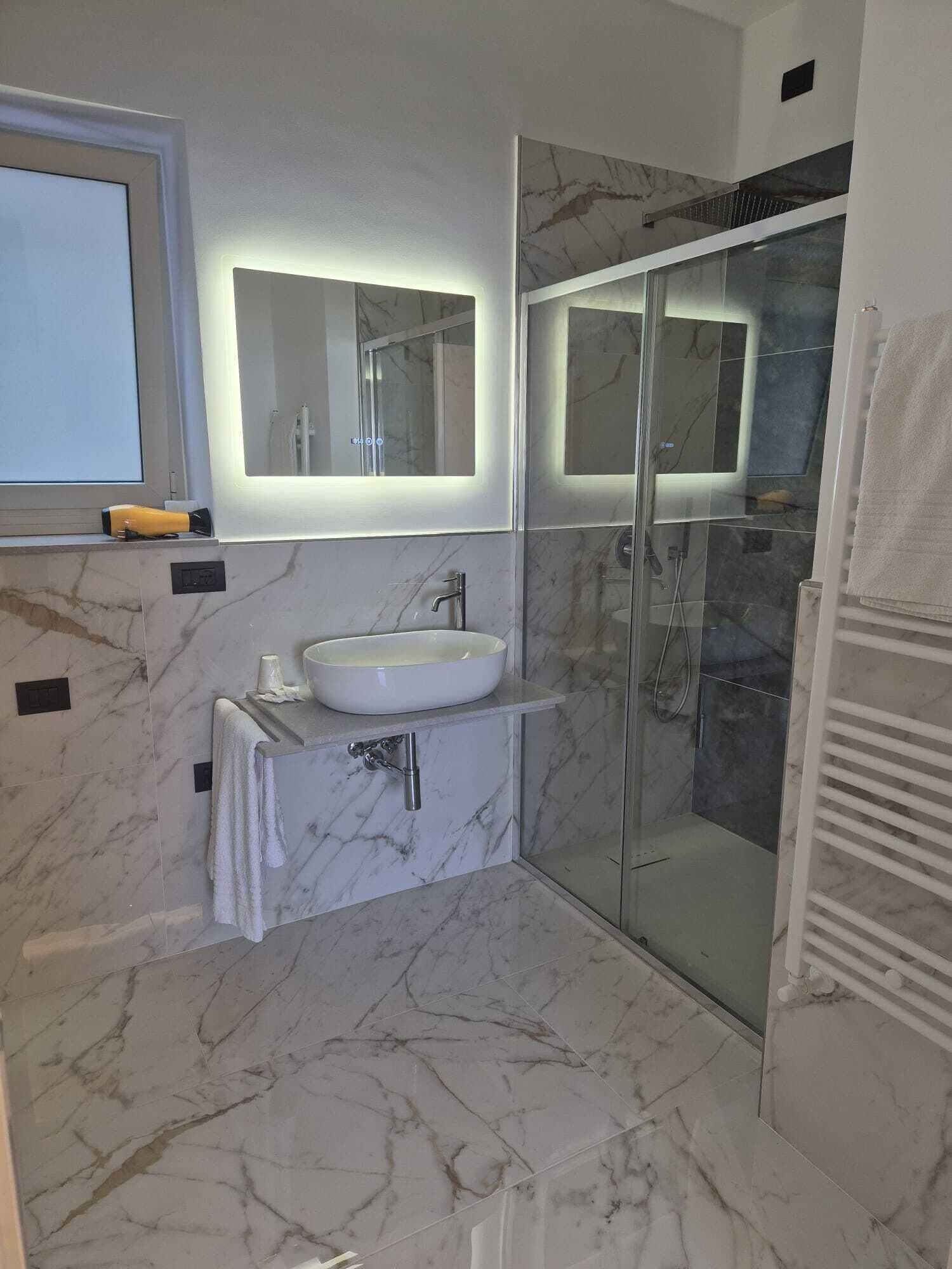 A modern bathroom with a marble sink, a glass shower enclosure, and a large mirror.