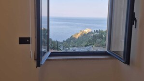 Una habitació amb un gran finestral, un sòl de marbre i vistes a un paisatge costaner.