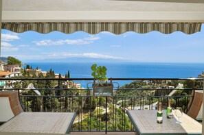 A balcony with a view of the sea, a potted plant, and two wine glasses and bottles on the table. - Hotel Condor (Taormina)