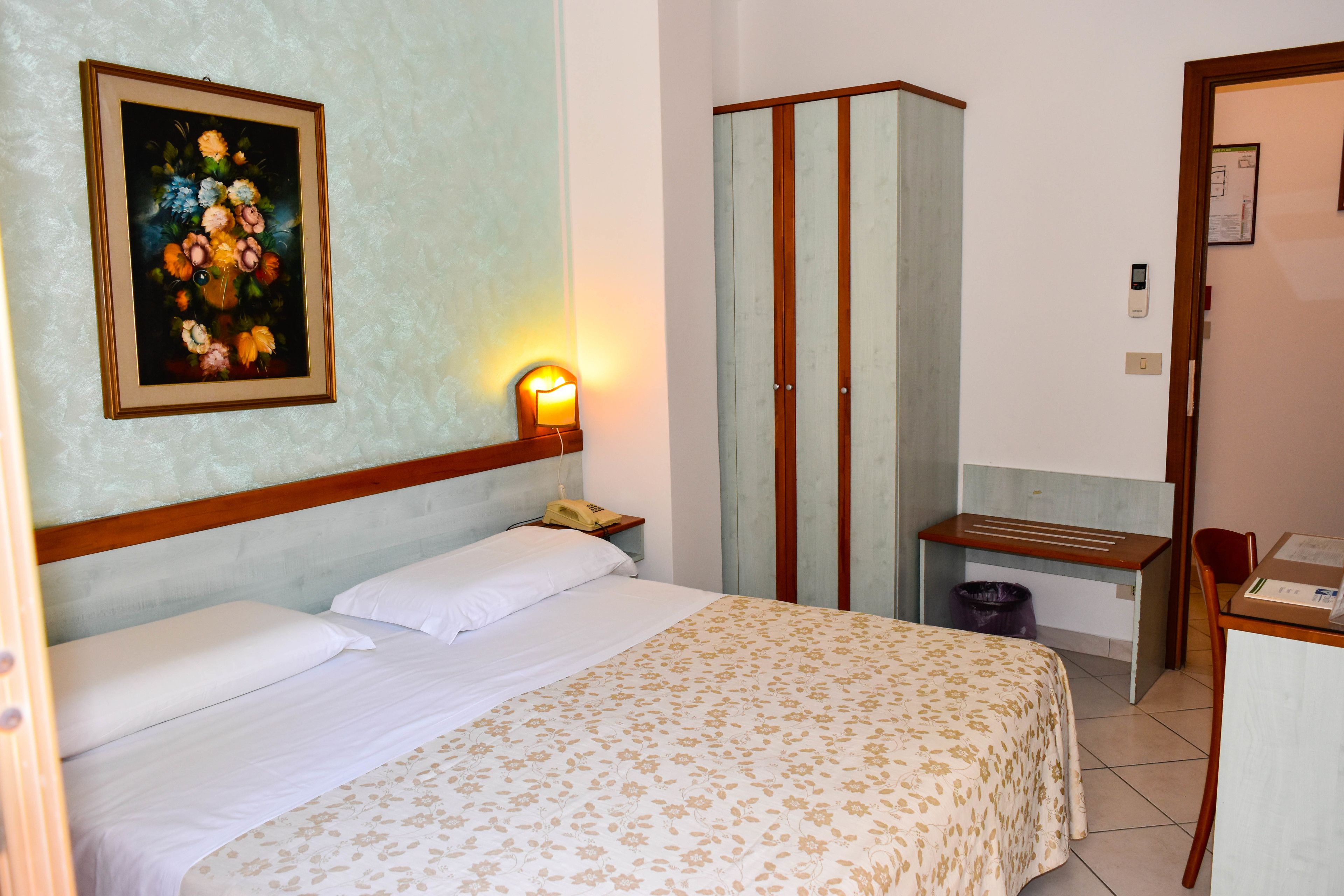 Una camera d'albergo con un letto, una scrivania, un armadio e un quadro appeso al muro.
