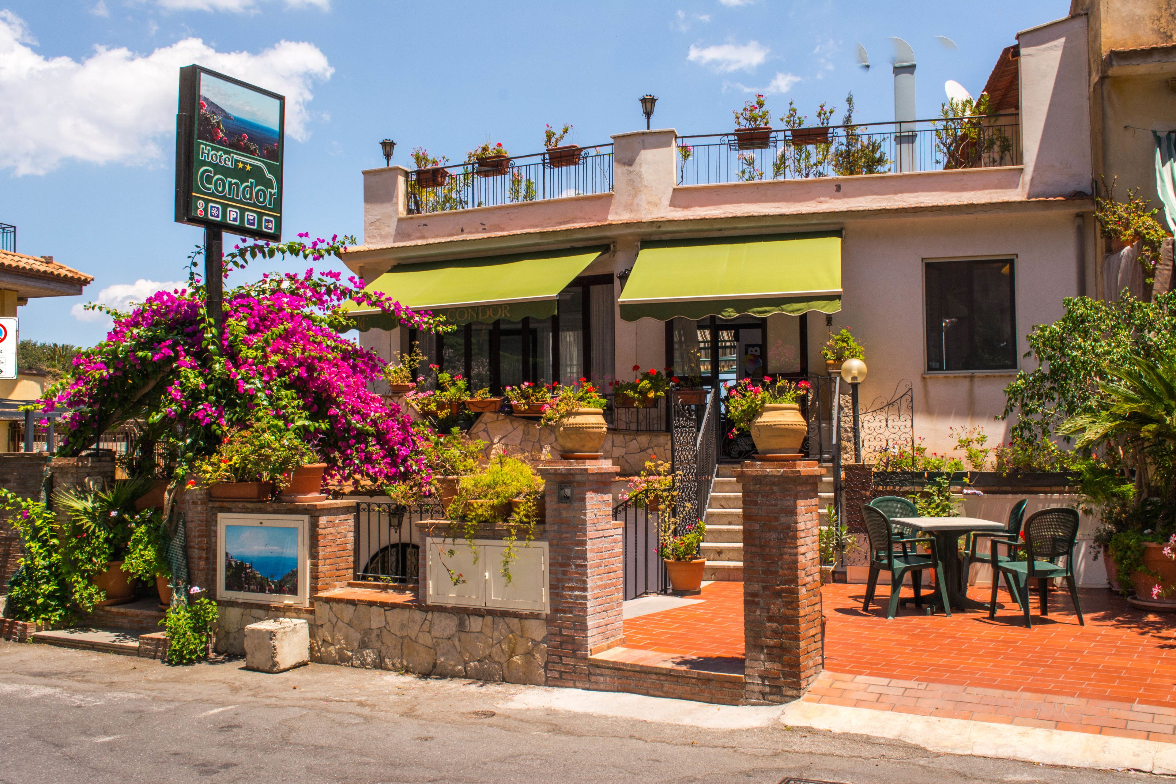 A hotel with a green awning, outdoor seating, and potted plants.