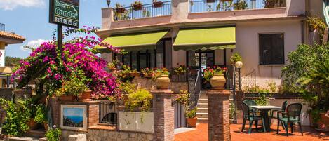 Un hotel con toldo verde, mobiliario exterior y plantas en macetas.