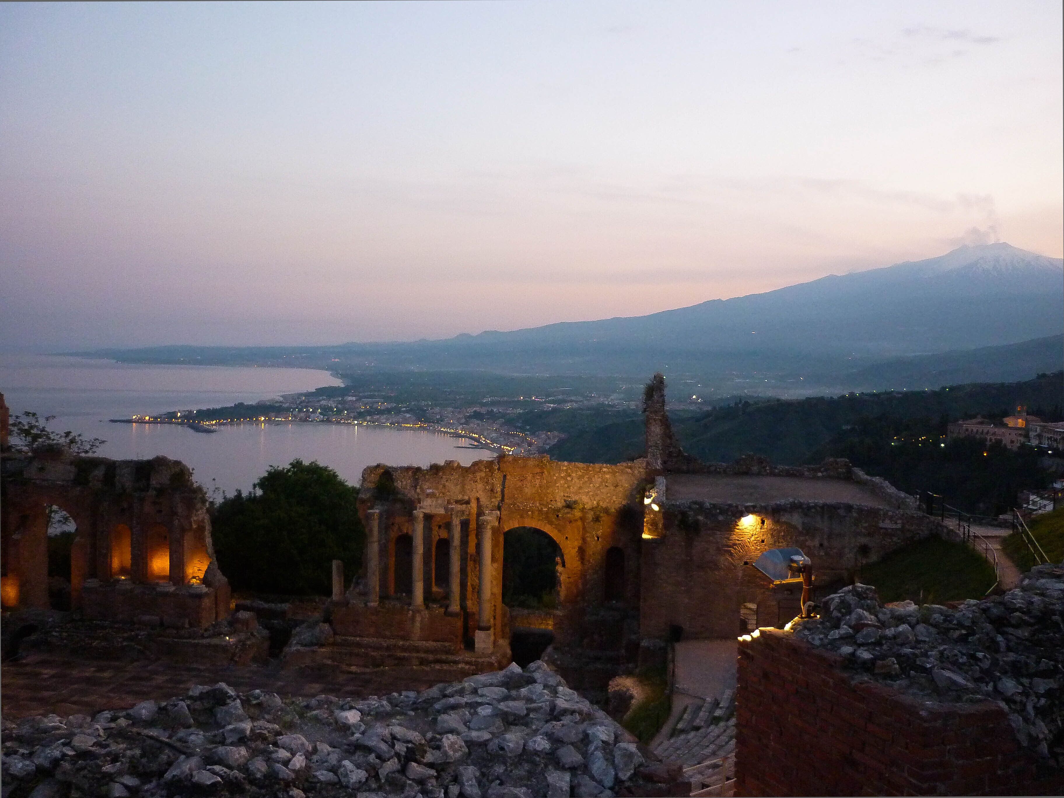 A historic site with ancient ruins and a view of a distant city and mountain.