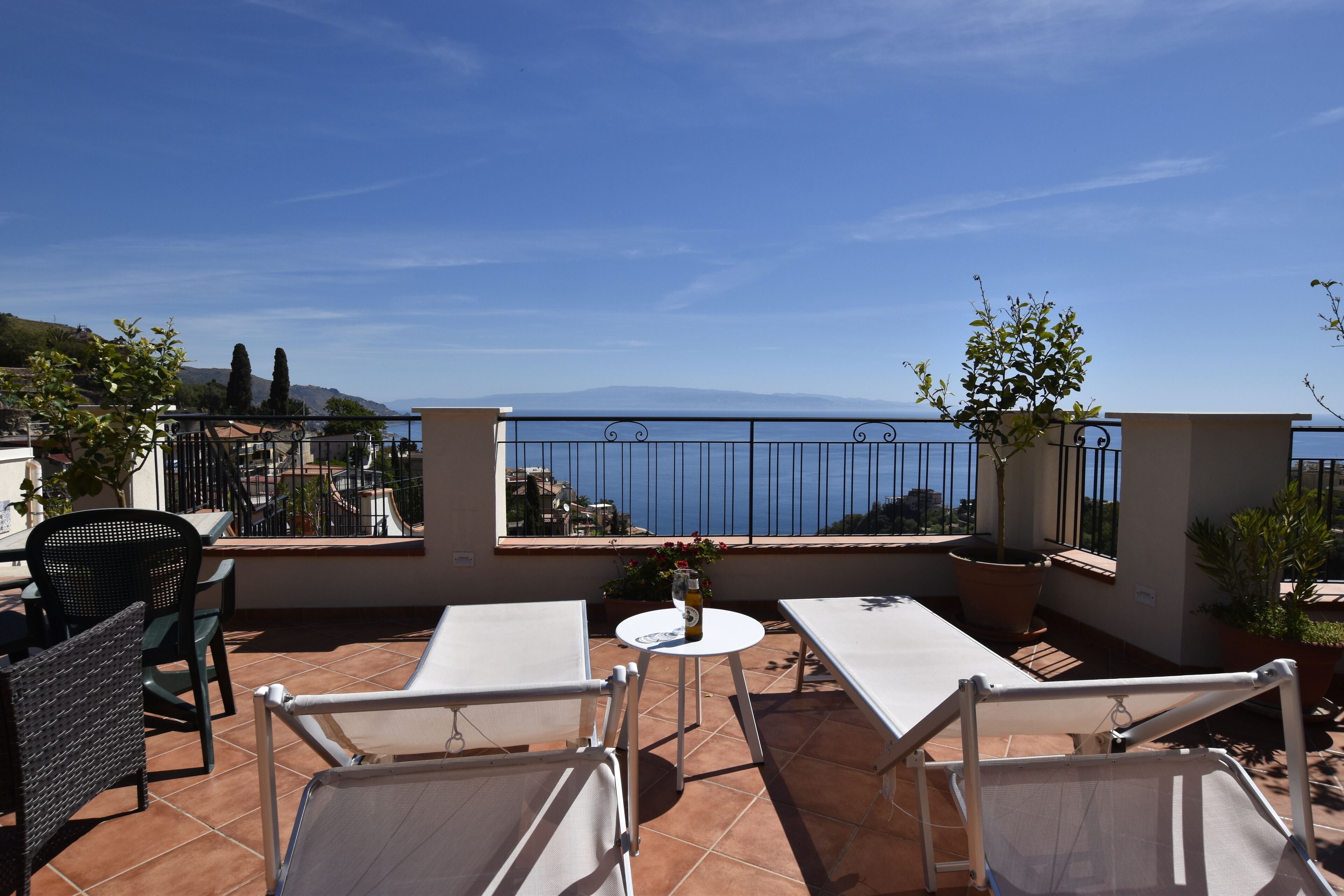 Eine Terrasse mit weißen Tischen und Stühlen, Blumentöpfen und Blick aufs Meer.