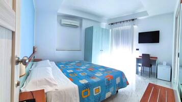 A hotel room with a bed, a desk, a chair, a TV, and an air conditioning unit.
