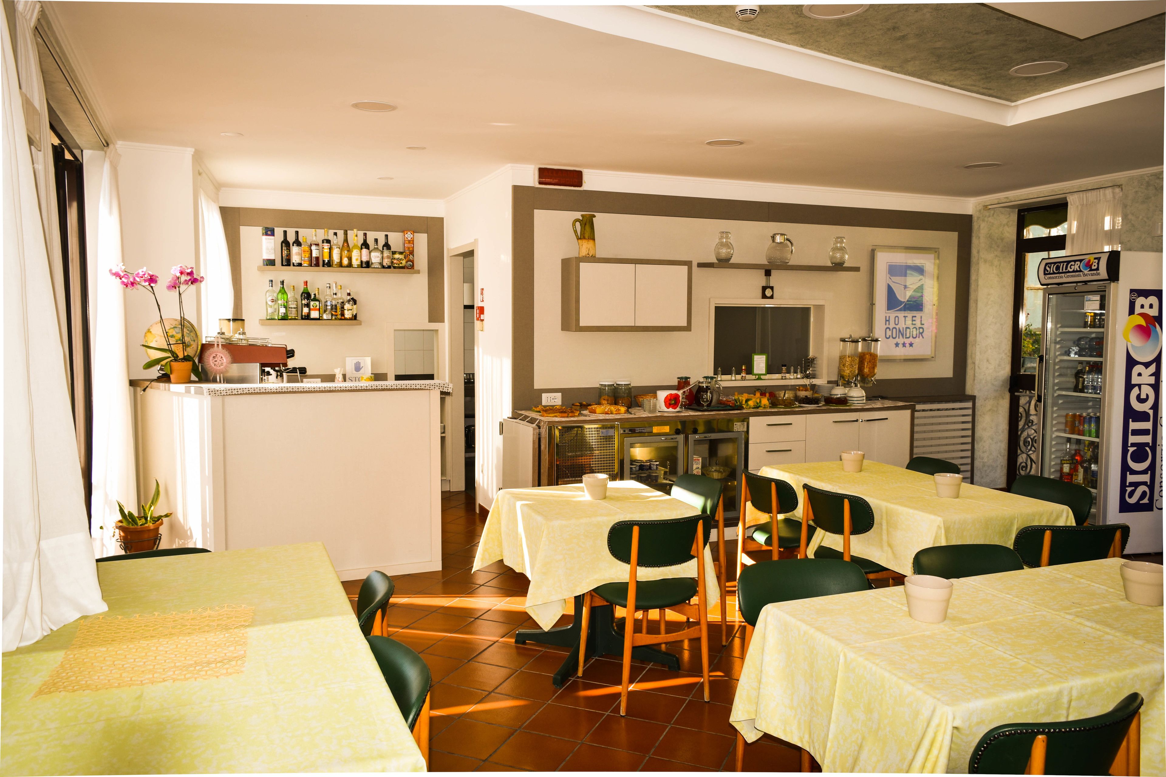 A hotel restaurant with multiple tables, chairs, a bar area, and a refrigerator.