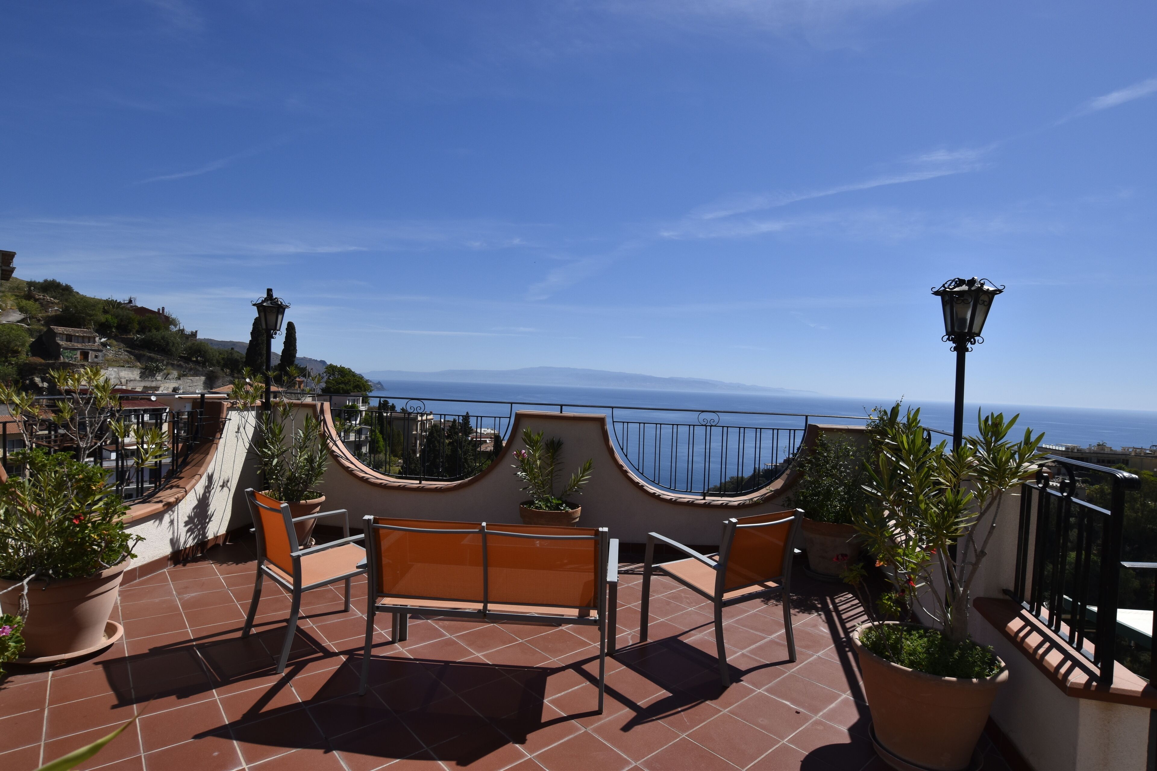 A terrace with a bench, potted plants, and a view of the sea.