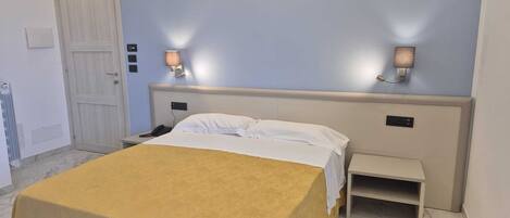 A hotel room with a bed, bedside table, lamp, and a door.