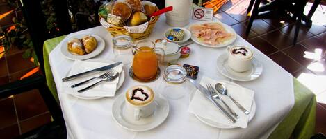 A breakfast table with a variety of pastries, a jug of orange juice, and coffee cups.