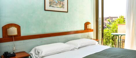 Habitación de hotel con cama, teléfono en la mesita de noche, un cuadro en la pared y vistas al exterior.