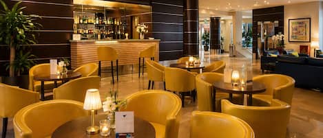 A hotel lobby with yellow seating, a bar area, and a reception desk.
