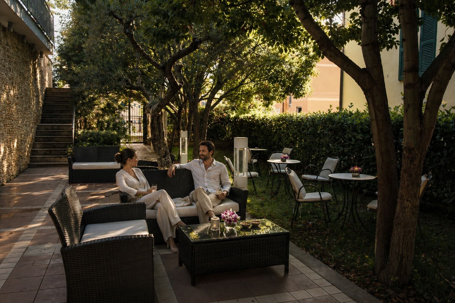 An outdoor seating area with wicker furniture, a glass-top table, and a staircase leading to an upper level.