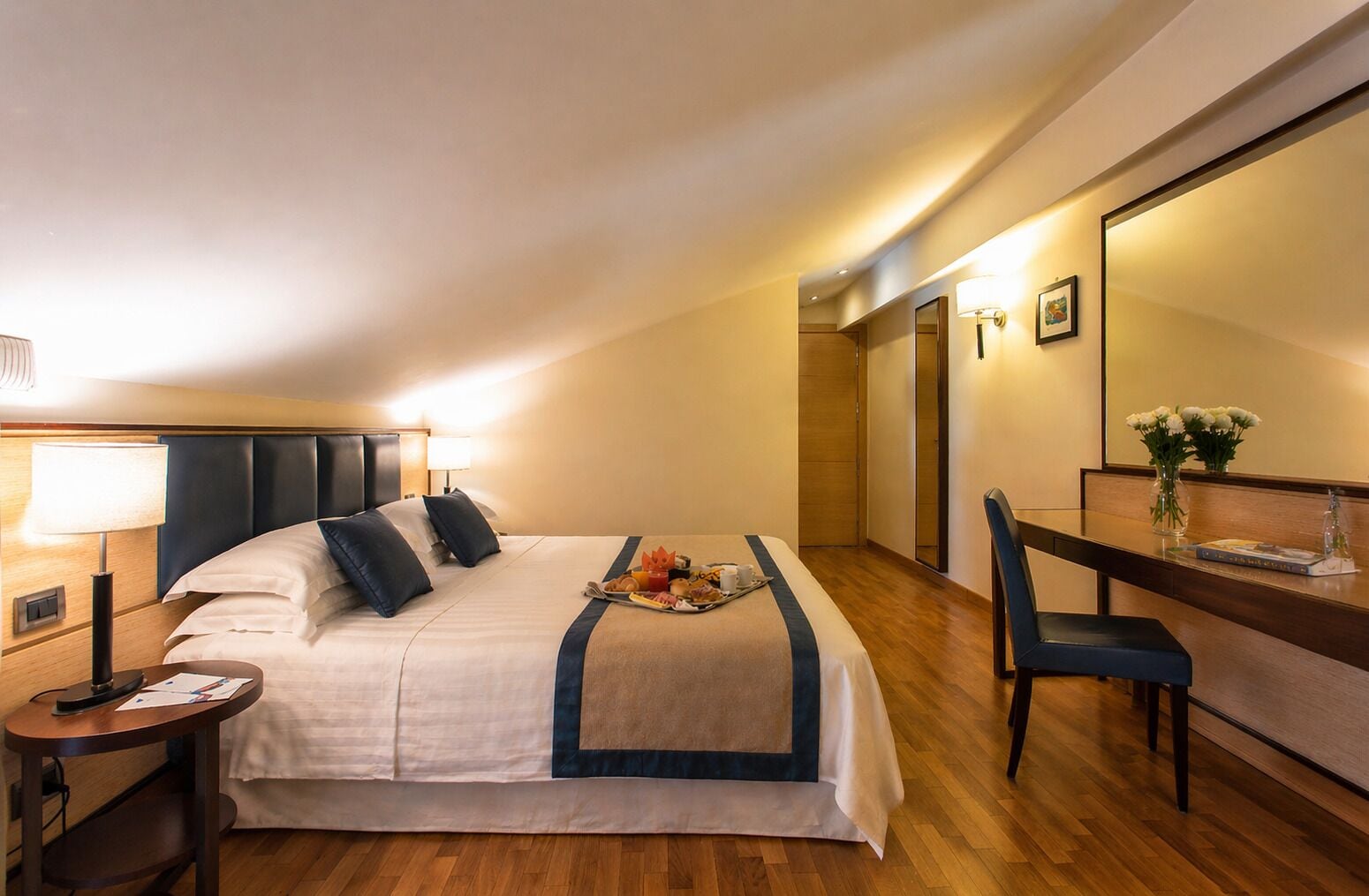 Una habitación de hotel con cama, mesita de noche, escritorio, silla y espejo.