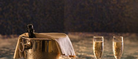 A spa setting with a hot tub, two champagne glasses, a candle, and a towel on a tiled surface.