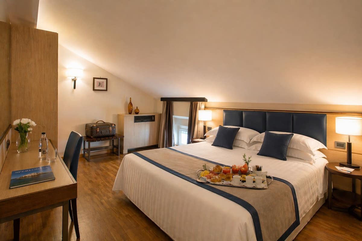 A hotel room with a large bed, bedside tables, a desk, and a dining table.