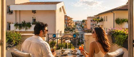Un couple est assis à une table en plein air, avec vue sur une rue bordant la côte.