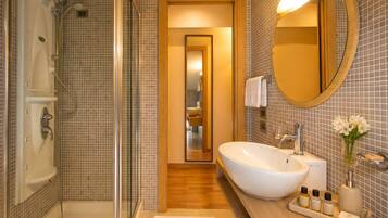 Un bagno con doccia vetrata, un lavabo bianco di grandi dimensioni, uno specchio rotondo e un mobile vanitario in legno.