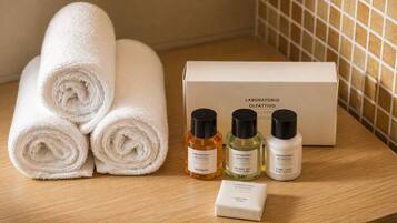 Neatly rolled white towels, three bottles of body care products, and a box labeled 'LABORATORIO OLFATTIVO' on a wooden surface.
