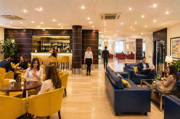 A hotel lobby with yellow chairs, blue sofas, a bar area, and a reception desk.
