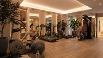 Un gimnasio con máquinas de cardio, una máquina de remo y una silla de masajes.