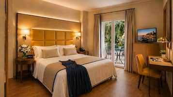 A hotel room with a large bed, a desk, a chair, a TV, and a balcony with a view.