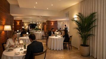 Un comedor de hotel con mesas redondas, personal de servicio y una planta grande en maceta.