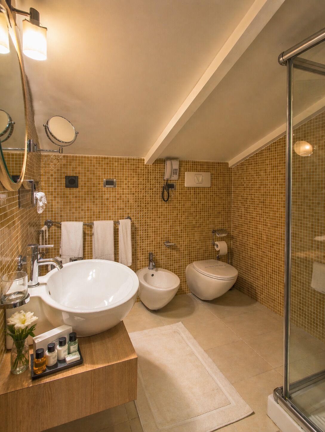 A bathroom with a large sink, bidet, and toilet, a mirror, and a phone.