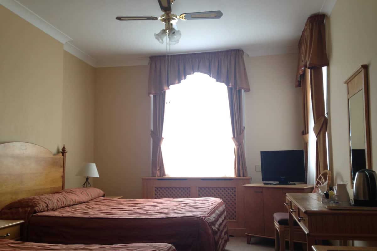 A hotel room with two beds, a desk, a television, and a ceiling fan.