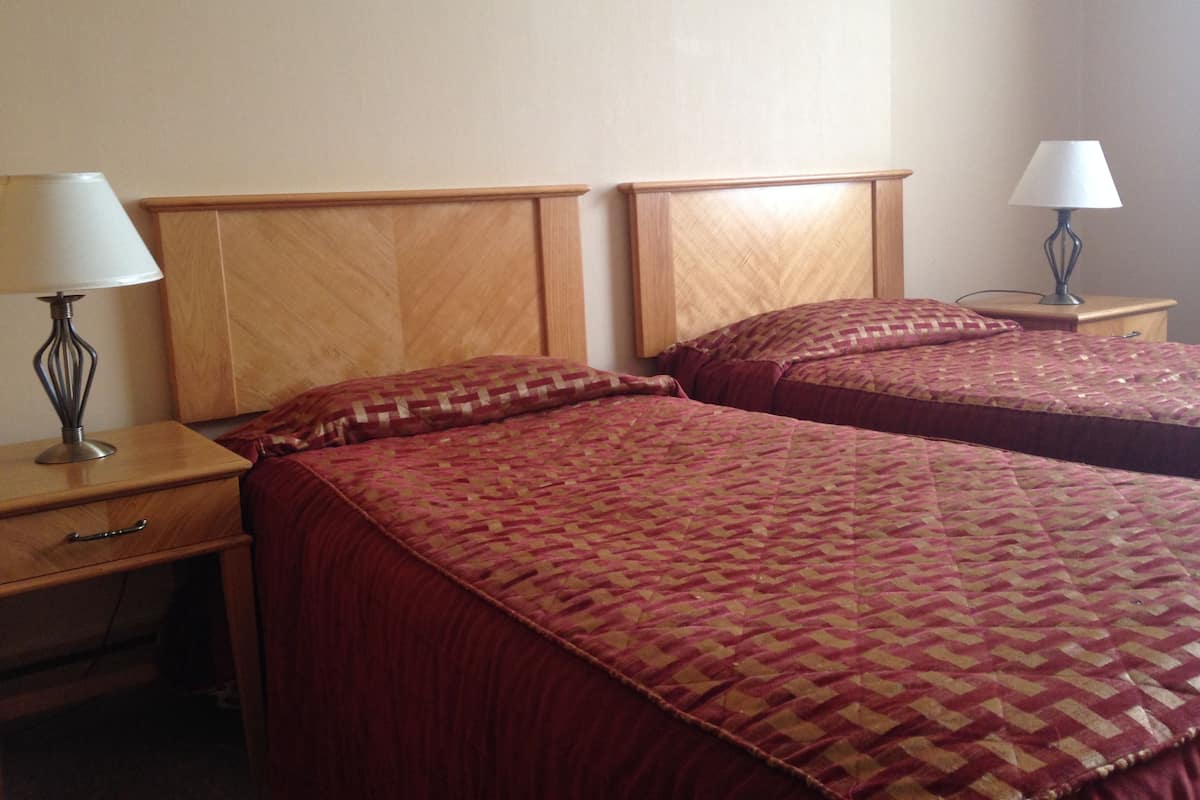 A hotel room with two beds, each with a wooden headboard and a matching nightstand.