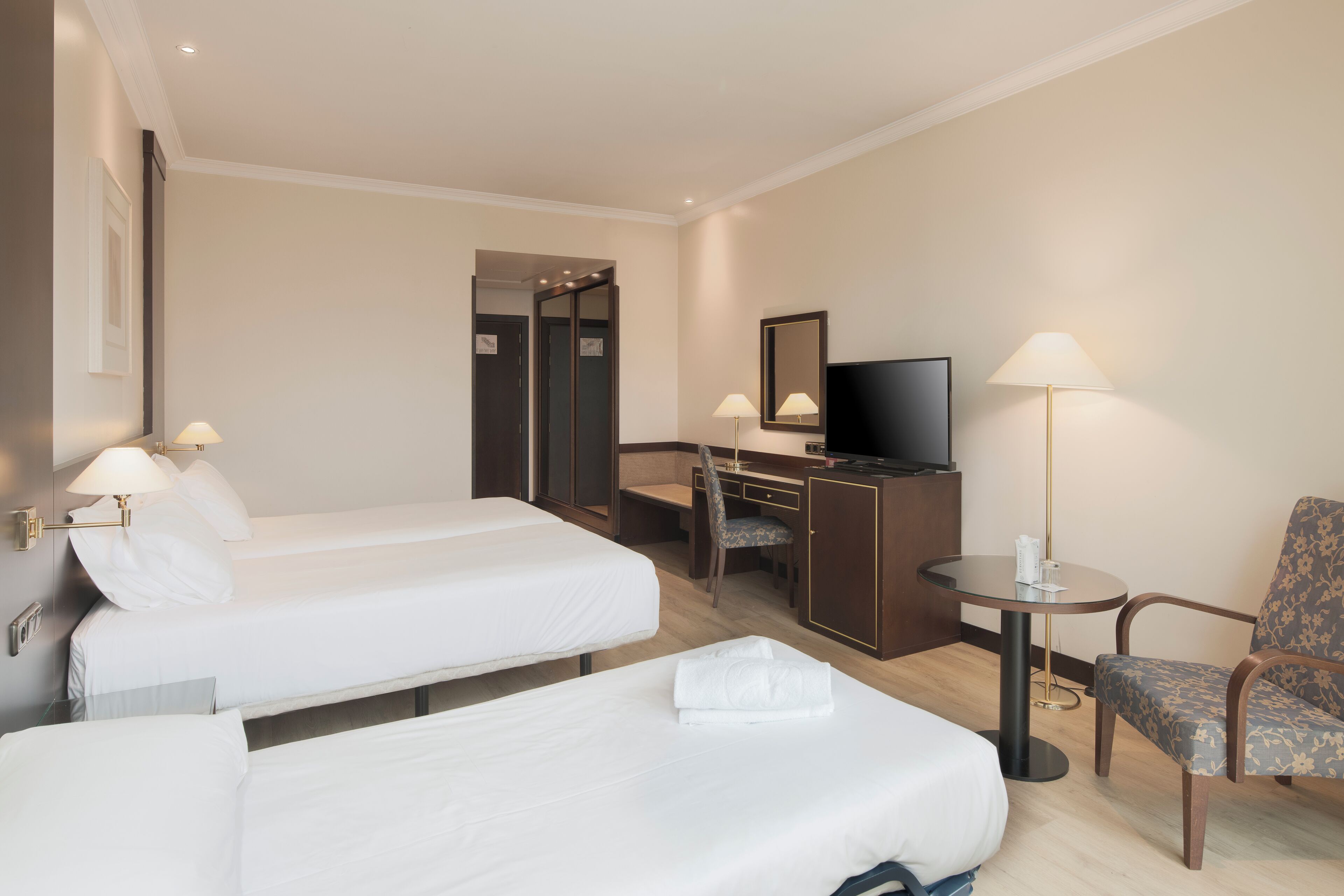 A hotel room with two beds, a desk with a chair, a television, and a lamp.