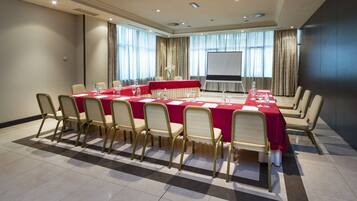 A conference room with a long table, chairs, a projector screen, and a large window with curtains.