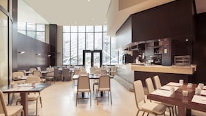 Un moderno comedor con mesas y sillas, una encimera de cocina y grandes ventanales con vista a la ciudad.