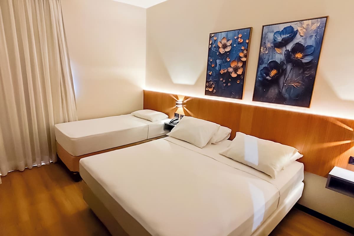 Une chambre d’hôtel avec un lit double, un lit simple, une table de chevet, une lampe et deux tableaux au mur.