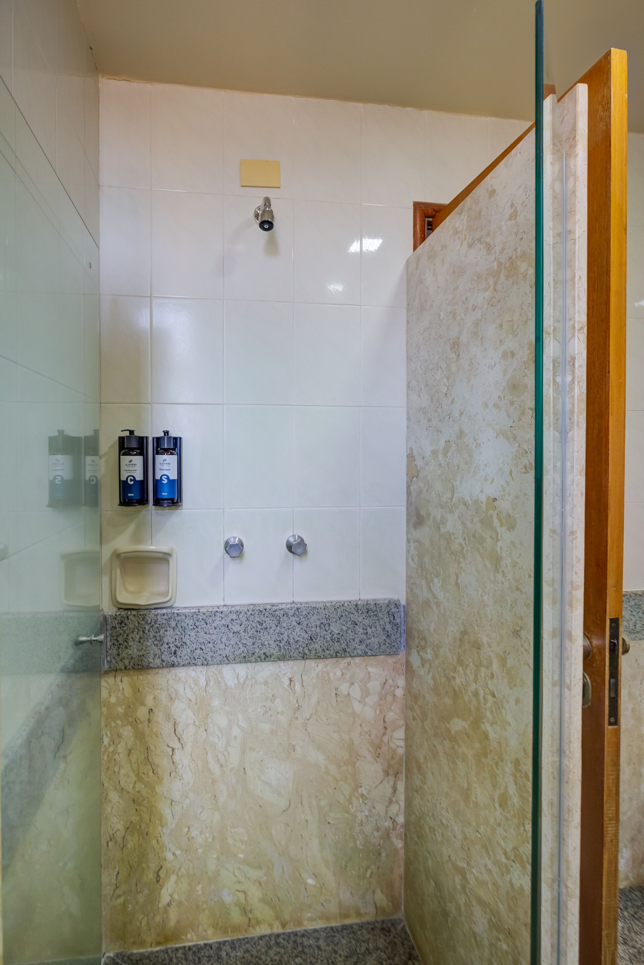 A bathroom with white tiled walls, a marble countertop, and a glass shower enclosure.