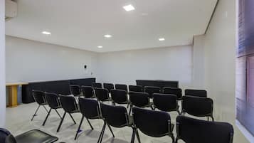 A conference room with rows of black chairs, a podium, and a large window with blinds.