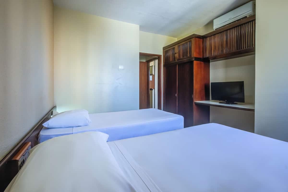 Une chambre d’hôtel avec deux lits simples, un téléviseur posé sur un meuble en bois et une armoire.
