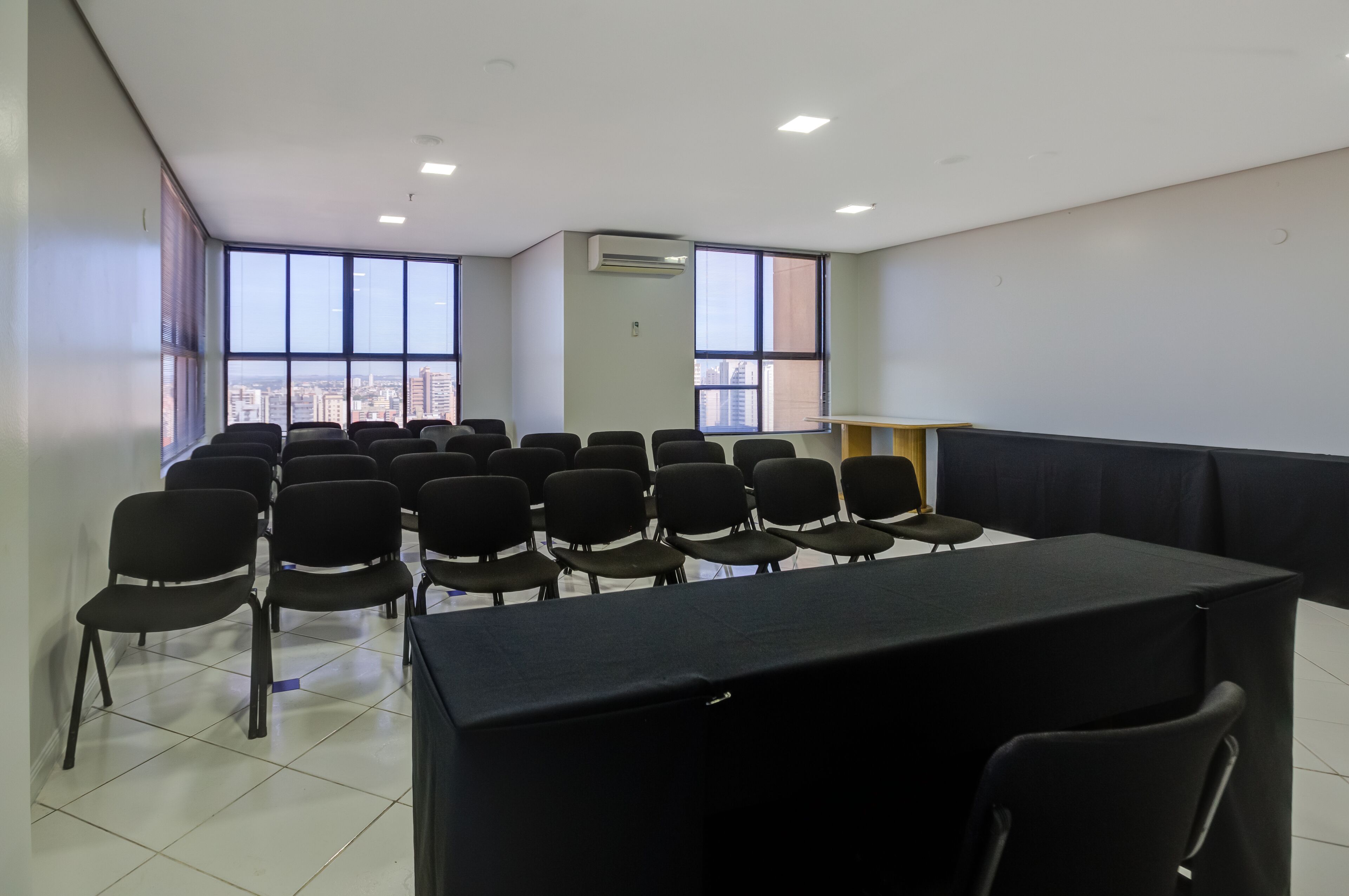 A conference room with rows of chairs, a table, and large windows with a city view.