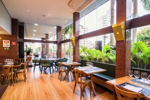 A restaurant with wooden tables and chairs, large windows with a view of palm trees and buildings, and a modern interior design. - SLAVIERO Londrina (Londrina)