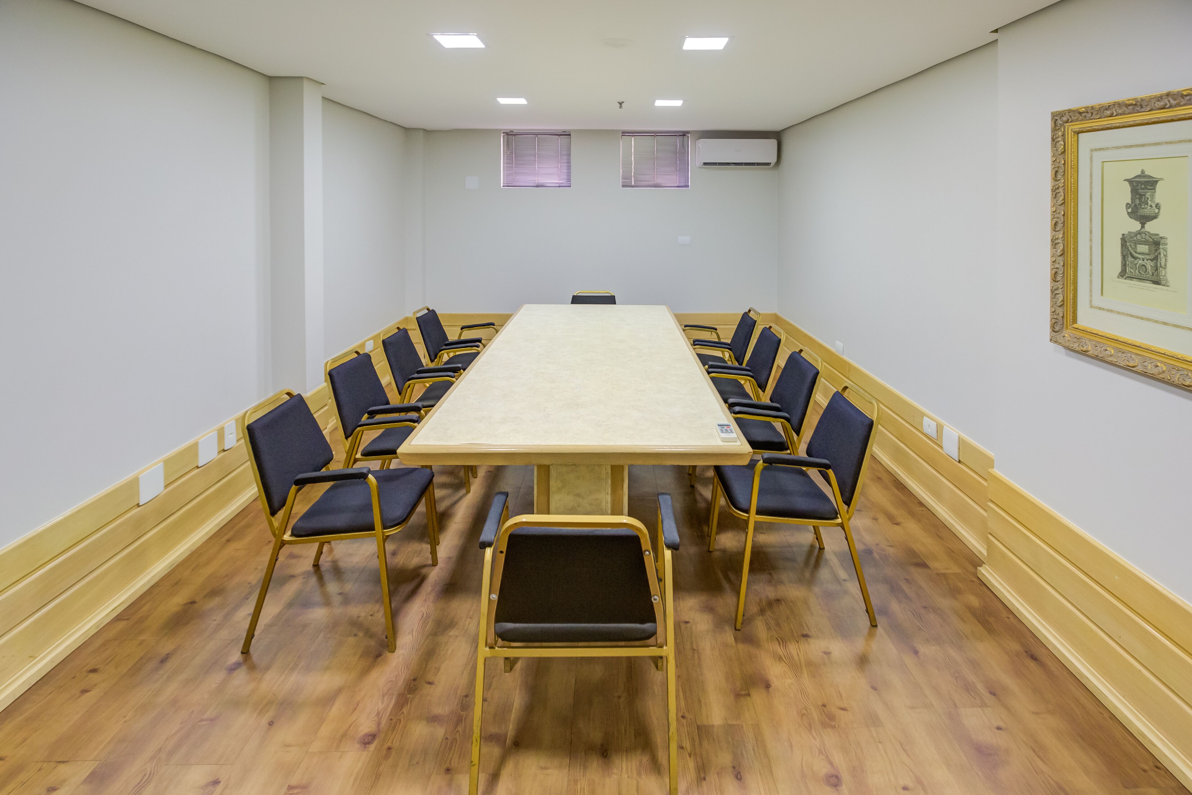 A conference room with a large rectangular table surrounded by chairs, wooden flooring, and a framed picture on the wall.