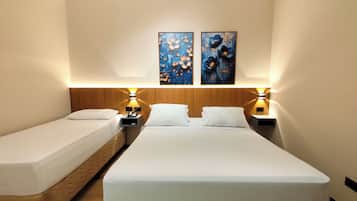 A hotel room with two single beds, a wooden headboard, bedside lamps, and two wall-mounted paintings.